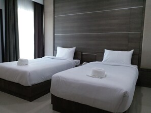 Dos camas individuales con ropa de cama y almohadas blancas, cabecera oscura y ventana con cortinas.