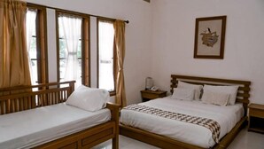 A room with two wooden beds, a bedside table with a lamp, and a framed picture on the wall. - Grand Cepu Hotel (Cepu)