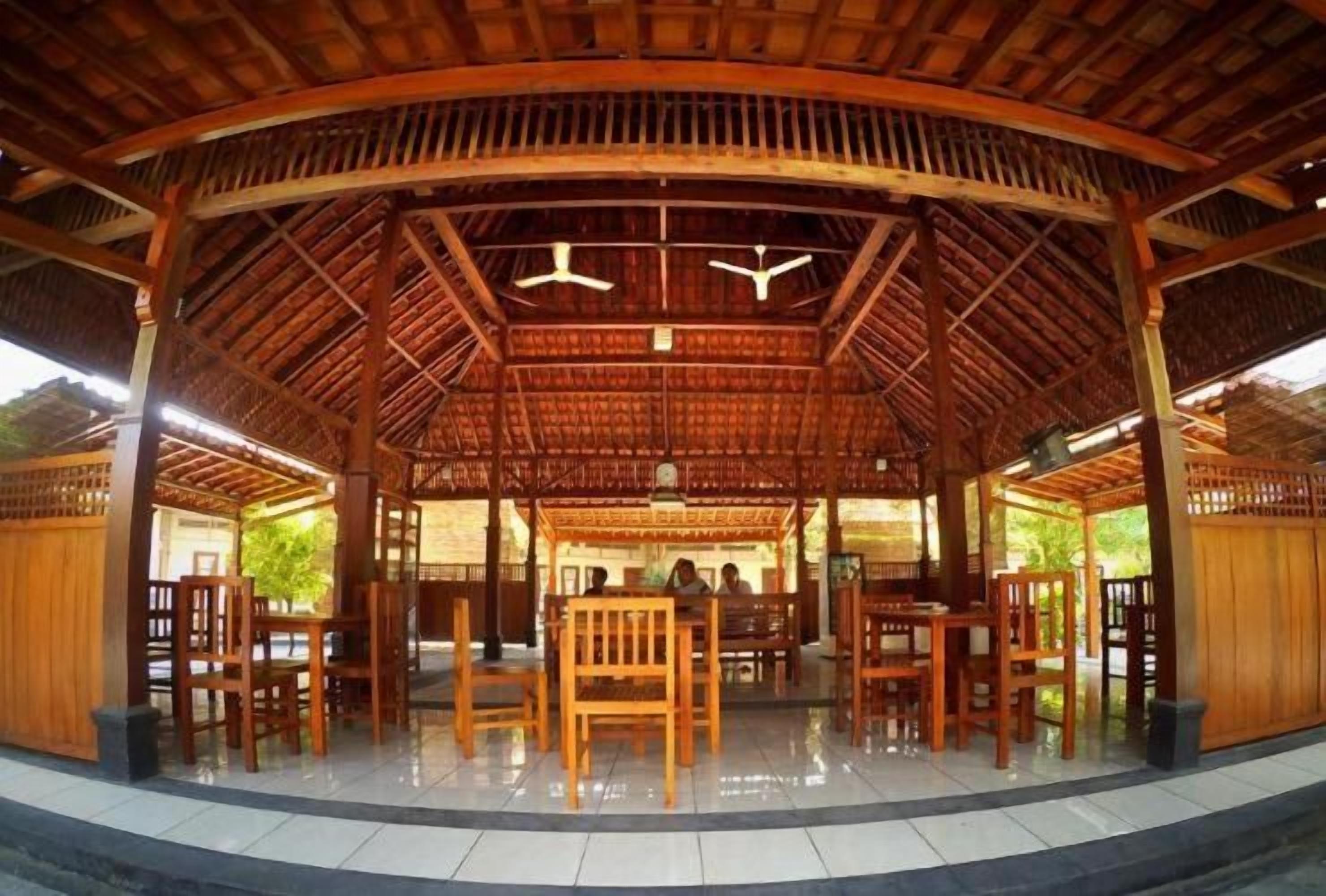A covered pavilion with a wooden roof, several wooden chairs, and a central table.
