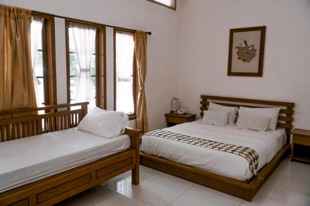 A double bed with a wooden frame and white bedding, a bedside table with a lamp, and a window with curtains.