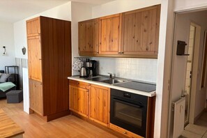 A compact kitchen with wooden cabinets, a black dishwasher, and a tiled backsplash. - House Sanddorn, Apartment 1 (Großenbrode)