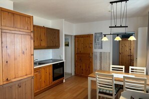 A kitchen with wooden cabinets, a sink, and a dining area with chairs and a table. - House Sanddorn, Apartment 1 (Großenbrode)