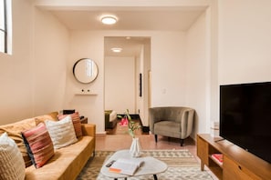 Ein Wohnzimmer mit einer Couch, einem Sessel, einem Couchtisch und einem Flachbildfernseher.