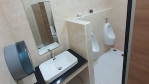 Un baño moderno con lavamanos, espejo, orinales y un cubo de basura.