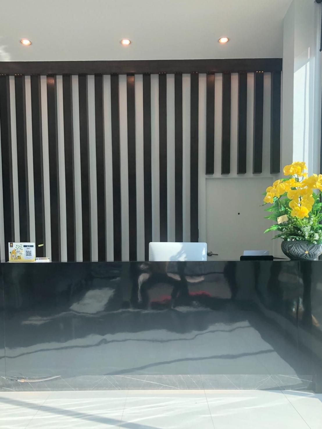 A reception area with a black and white striped wall, a reception desk, and a potted plant with yellow flowers.