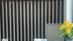 Un área de recepción con una pared a rayas blancas y negras, un mostrador de recepción y una planta en maceta con flores amarillas.
