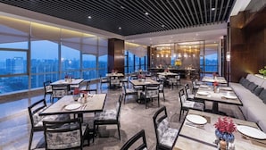 A modern dining area with tables and chairs, large windows, and a city view. - New Century Hotel Binjiang Hangzhou (Hangzhou)