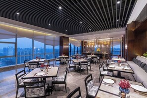 A modern dining area with tables and chairs, large windows, and a city view. - New Century Hotel Binjiang Hangzhou (Hangzhou)