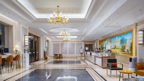 En hotellobby med ett marmorgolv, en receptionsdisk, en tavla på väggen och en kristallkrona.