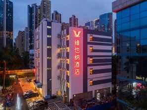 Un hotel amb un senyal de neó destacat, envoltat d'edificis alts i una zona d'aparcament.