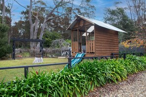 A wooden cabin with a porch and a slide, surrounded by a fence and lush greenery. - Old Majors Family 4-Bed Retreat Southern Highlands (Braemar)