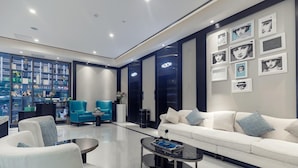 Un salon moderne avec un canapé blanc, des fauteuils bleus, une table basse et une bibliothèque remplie d’objets décoratifs.