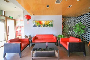 A reception area with a red sofa set, a coffee table, a painting of a landscape, and a red lantern.