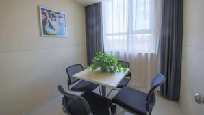 Ein Zimmer mit Esstisch und vier Stühlen, einer Topfpflanze auf dem Tisch, einem Bild an der Wand und einem Fenster mit Vorhängen.