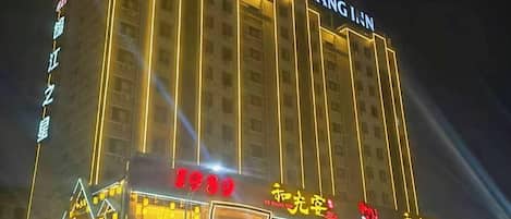 Un hotel de varios pisos con señalización iluminada, una entrada destacada y un área de estacionamiento al frente.