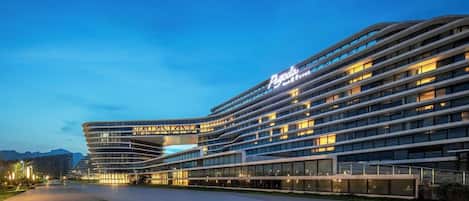 A modern hotel with a curved facade, multiple floors, and a well-lit entrance area.