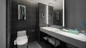 Et moderne badeværelse med toilet, stort spejl og en lang kommode med vask og håndklæder.