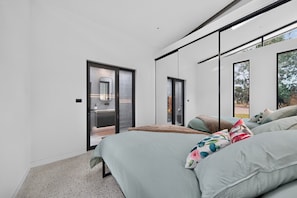 A modern bedroom with a large bed, a sliding glass door leading to a bathroom, and a view of the outdoors.