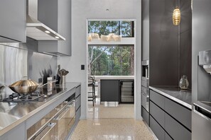 A modern kitchen with stainless steel appliances, a large window, and a view of trees.