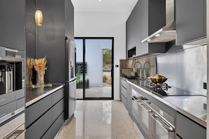 A modern kitchen with stainless steel appliances, a glass door leading to an outdoor area, and a minimalist design.
