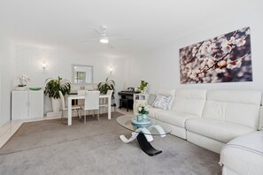 Ein modernes Wohnzimmer mit einem weißen Sofa, einem Glastisch und einem Essbereich mit weißen Stühlen und einem Klavier.