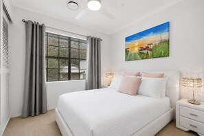A bedroom with a large bed, a window with blinds, a painting, and a nightstand with a lamp. - Spacious 3-Bedroom Townhouse Near Terrigal Beach (Terrigal)
