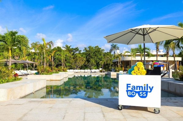 A poolside area with lounge chairs, a water feature, and a cart labeled 'Family Boss' with towels. - Family Selection At Grand Palladium Kantenah Resort & Spa (Kantenah)