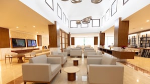 A spacious lobby with multiple seating areas, a reception desk, and a large screen displaying information. - Family Selection At Grand Palladium Kantenah Resort & Spa (Kantenah)