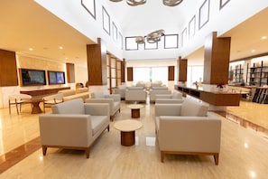 A spacious lobby with multiple seating areas, a reception desk, and a large screen displaying information. - Family Selection At Grand Palladium Kantenah Resort & Spa (Kantenah)