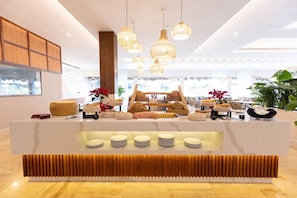 A modern reception area with a central counter displaying food items, surrounded by hanging pendant lights. - Family Selection At Grand Palladium Kantenah Resort & Spa (Kantenah)