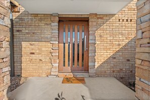 Ein Gebäude aus Ziegelsteinen mit einem Holztürrahmen, einer Fußmatte und einem Betonweg.