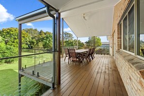 Ein überdachter Außenbereich mit Holzterrasse, Tisch und Stühlen und Blick auf eine grüne Landschaft.