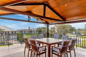 Eine überdachte Terrasse im Freien mit einem Holztisch und -stühlen, einem Geländer und Blick auf Wohnhäuser.