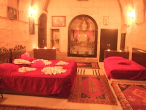 A room with a fireplace, two beds, and a rug. - Kapadokya Ihlara Konaklari Caves (Guzelyurt)