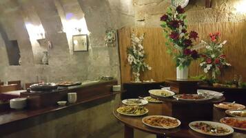 A dining area with multiple tables set for meals, a wooden wall with decorative elements, and a stone wall in the background.