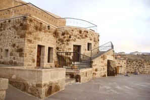 A stone building with a curved balcony and a staircase leading to an upper level. - Kapadokya Ihlara Konaklari Caves (Guzelyurt)