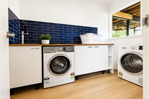 A compact laundry room with two washing machines, a sink, and a potted plant. - Coastal 3-Bed Haven With Panoramic Views (Portarlington)