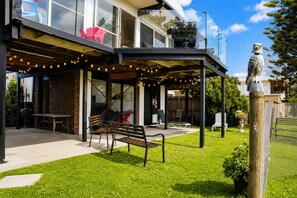 A modern outdoor seating area with a bench and chairs, a glass enclosure, and a statue. - Coastal 3-Bed Haven With Panoramic Views (Portarlington)