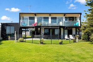A modern two-story building with a balcony, outdoor seating, and a fenced garden area. - Coastal 3-Bed Haven With Panoramic Views (Portarlington)