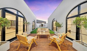 A modern outdoor patio with a wooden table and chairs, surrounded by large windows and potted plants. - Spacious 4-Bed Family House Near Gateway Plaza (Leopold)