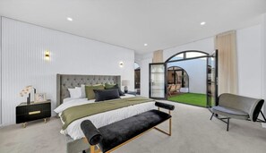 A modern bedroom with a large bed, a bench, a chair, and a view of a patio through glass doors. - Spacious 4-Bed Family House Near Gateway Plaza (Leopold)