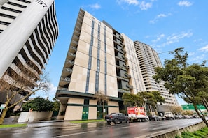 A multi-story building with a modern architectural design, featuring a prominent vertical element on the left side. - St Kilda Road 2-Bed With Rooftop Access (St Kilda)