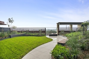 A modern outdoor space with a curved pathway, a grassy lawn, and a covered seating area. - Skyline 1-Bed Apartment Near Melbourne CBD (South Melbourne)