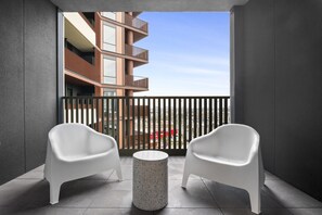 A balcony with two white chairs and a small table, overlooking a modern building with balconies. - Skyline 1-Bed Apartment Near Melbourne CBD (South Melbourne)