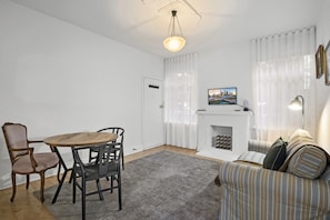 A living room with a fireplace, a dining table with chairs, a sofa, and a television mounted on the wall. - Poolside Art Deco Apartment in St Kilda West (Saint Kilda West)
