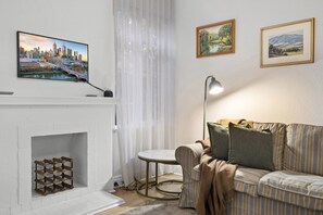 Ein Wohnzimmer mit Kamin, einer Couch, einem Tisch und zwei gerahmten Bildern an der Wand.