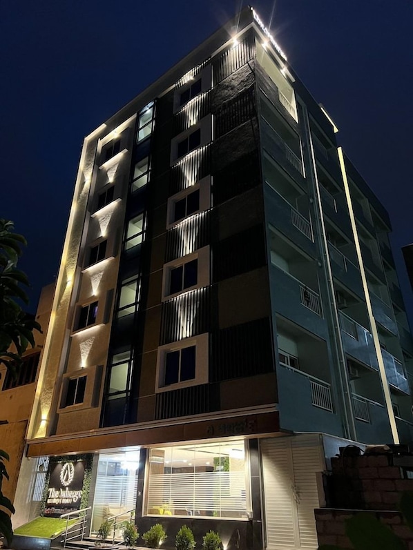 Un hotel de varios pisos con balcones, un restaurante en la planta baja y una fachada bien iluminada.