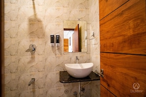 Un baño con pared de mármol, lavamanos blanco y puerta de madera.