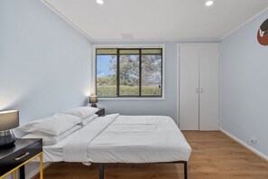 A bedroom with a bed, bedside table, lamp, window, and wardrobe. - Family-Friendly 3-Bed House in Kambah (Kambah)
