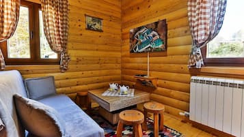 A cozy cabin interior with a sofa, a table with a teapot, a painting, and a window with curtains.